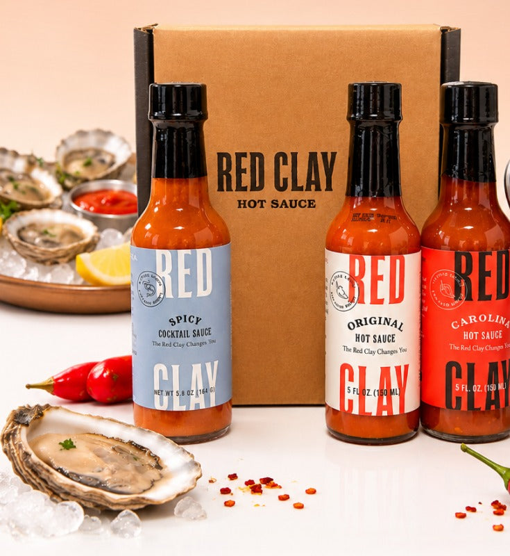 Red Clay Oyster Trio gift box with Spicy Cocktail Sauce, Original Hot Sauce, and Carolina Hot Sauce beside fresh oysters