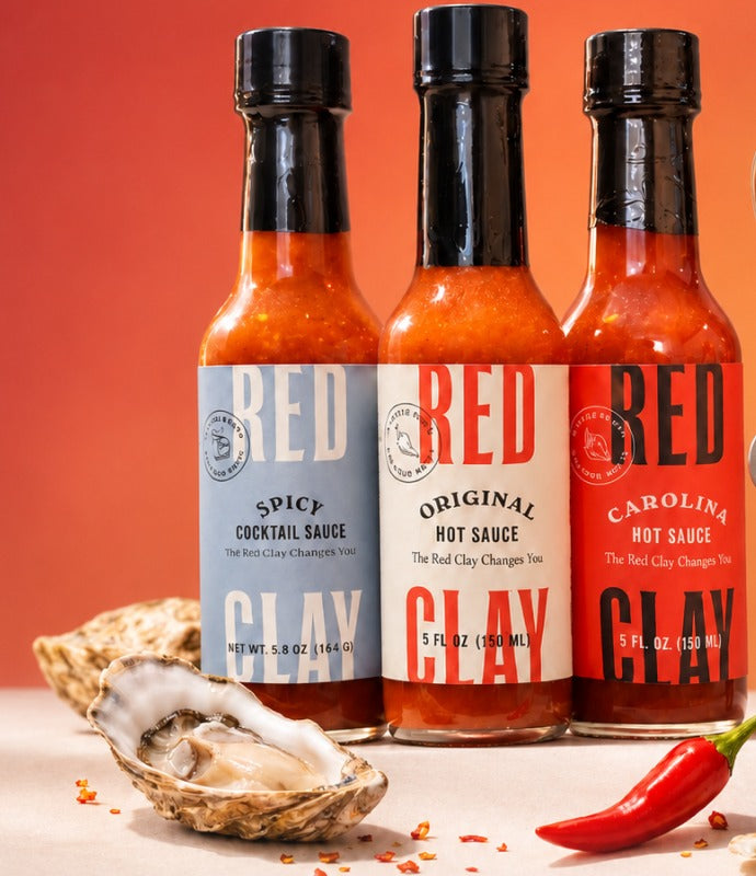 Spicy Cocktail Sauce, Original Hot Sauce, and Carolina Hot Sauce lined up with a shucked oyster and fresno chile