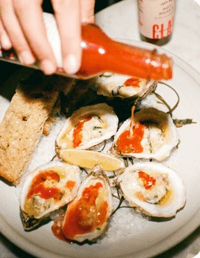 Red Clay hot sauce dashed over a plate of oysters with bread and lemon