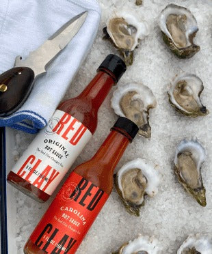 Original and Carolina Hot Sauce on a tray of raw oysters with an oyster knife